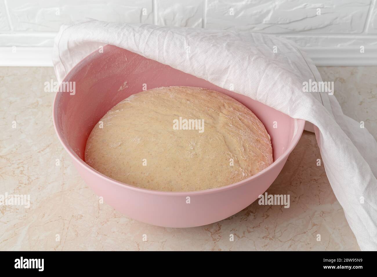 Frischer Hefeteig, der in einer großen Plastikschüssel mit weißem Leinentuch auf dem Küchentisch aufgeht. Hände Vorbereitung Teig zum Backen von hausgemachtem Brot. Stockfoto