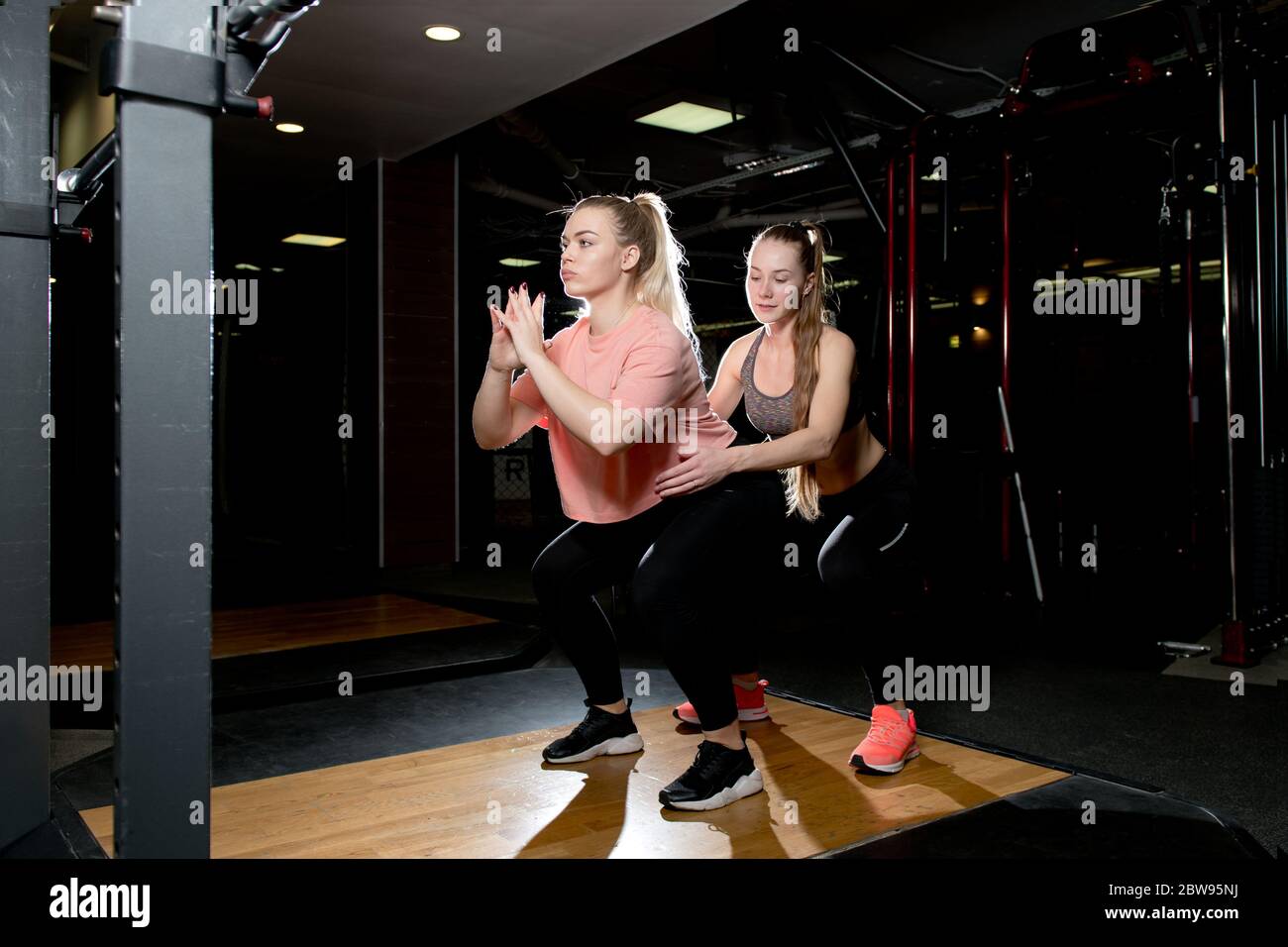 Mädchen hockt mit ihrem eigenen Gewicht unter der Kontrolle eines Trainers in einem Sportverein Stockfoto