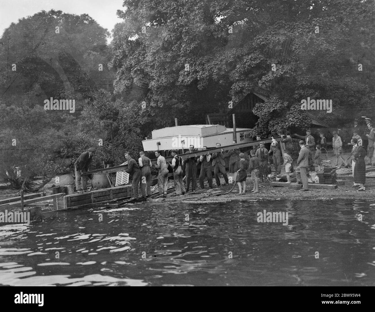 Geschwindigkeitsrekordtests wieder verschoben, wenn Miss England III Fouls Slipway . Kaye Don einen weiteren Schlaganfall von Unglück in seinem Versuch, den Weltrekord für die Wassergeschwindigkeit für Großbritannien in Miss England III gewinnen, Lord Wakefield ' s £ 40, 000 Speed boat, am Loch Lomond, Schottland, Als die Slipanlage, die zum Wasser führt, zusammenbrach und ein Loch im Rumpf des Bootes zerrissen wurde. Admiralty Taucher arbeiteten die ganze Nacht, um die Slipway zu ersetzen und machen eine Unterwasser-Untersuchung der Arbeit. Arbeiter bringen eine neue Schiene zum Ufer, um die gebrochene zu ersetzen, während ein Taucher bereit steht, um zu kommen Stockfoto