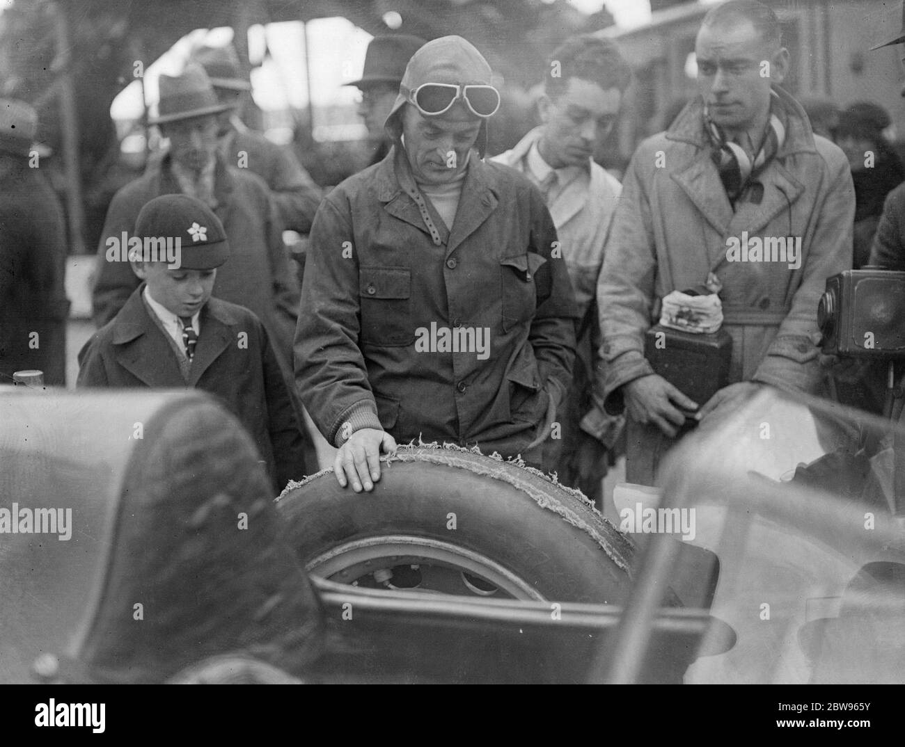 Sir Malcolm Campbell beschädigt Reifen auf Betonoberfläche der Brooklands-Strecke. Die Reifen wurden bei ihrem ersten und einzigen Auftritt auf der Brooklands-Strecke beim Eröffnungstreffen am Ostermontag von den Rädern des berühmten Bluebird-Autos abgezogen, als Sir Malcolm das berühmte Auto auf der Betonspur beschleunigte. Sir Malcolm Campbell untersucht einen der zerstörten Reifen des Bluebird nach dem Lauf. 28 März 1932 Stockfoto