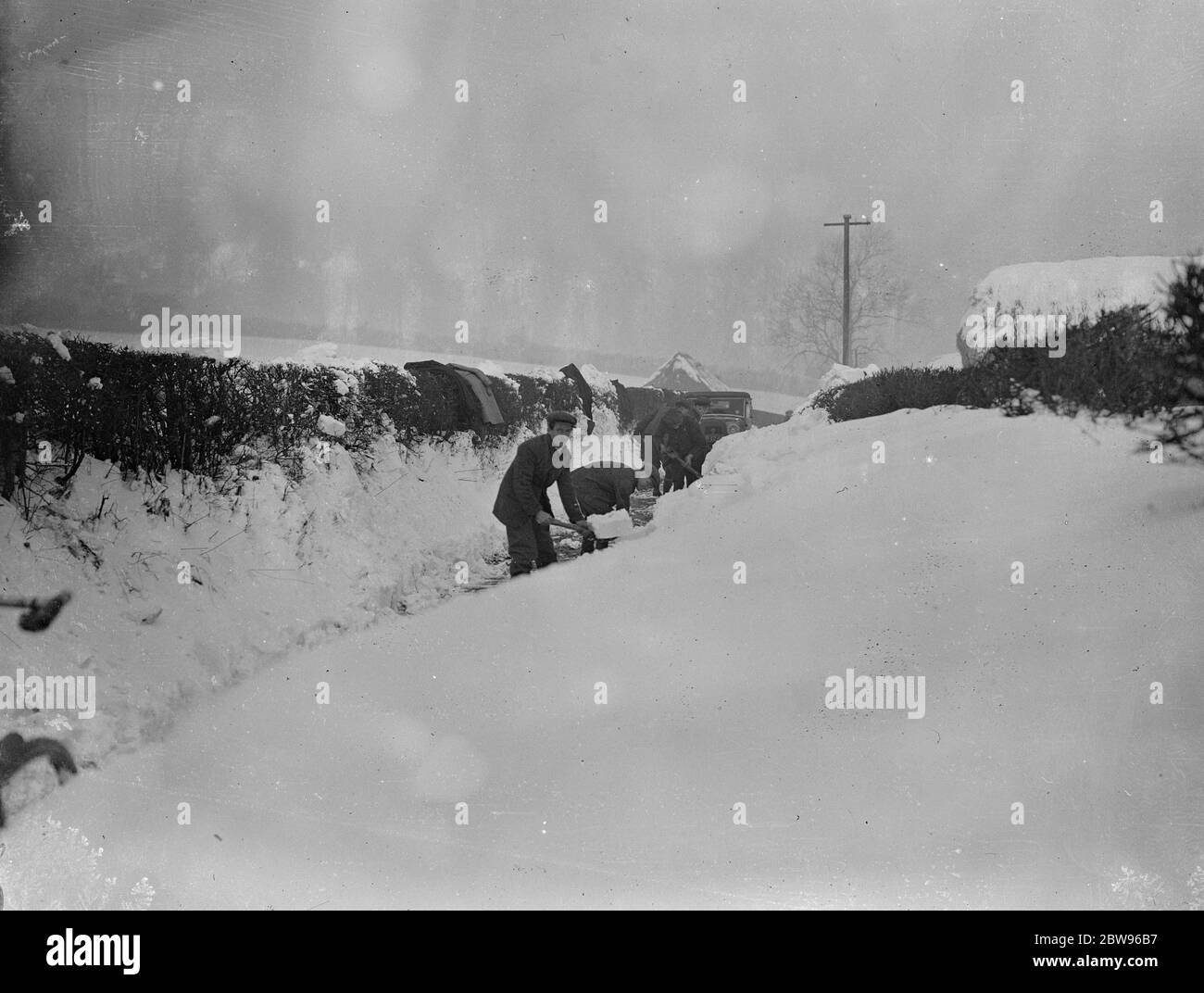 Drifts von Schnee vier Meter tief Block Surrey Straßen zum Verkehr. Drifts von Schnee mehr als vier Fuß in der Tiefe haben Straßen in Surrey und Kent blockiert und machte sie unpassierbar für den Verkehr, Armeen von Männern sind bei der Arbeit Clearing der Straßen. Schneeräumung auf einer Straße in Tatsfield, Surrey, wo Drifts sind mehr als vier Meter in der Tiefe. 13 Februar 1932 Stockfoto