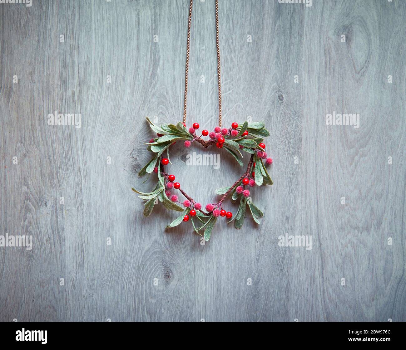 Weihnachtskranz in Form von Mistel mit roten Beeren hängen an rustikalen Holztür, traditionelle Weihnachtsschmuck. Minimalistische, trendige Weihnachtsdekoration. Stockfoto