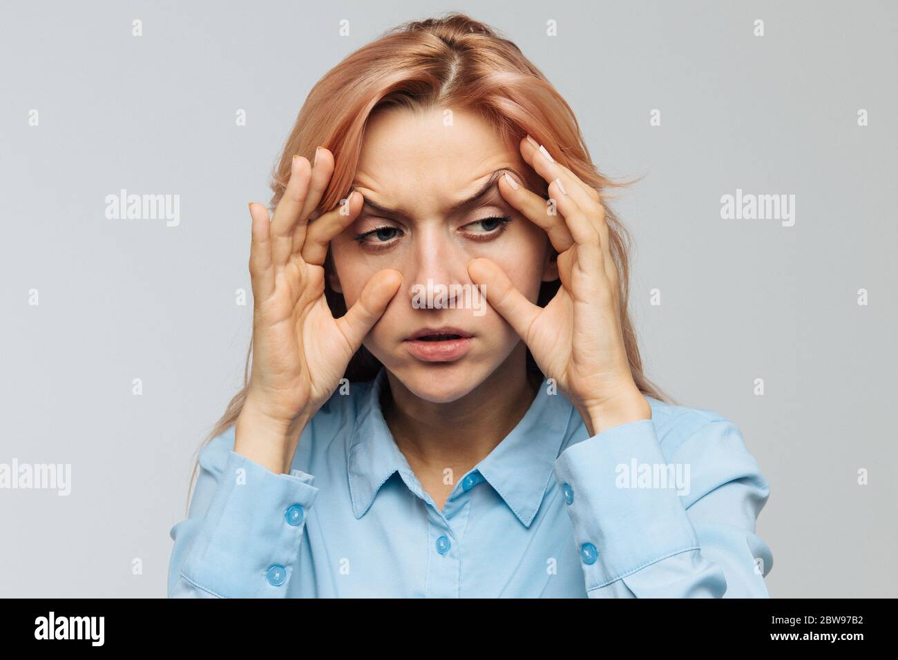 Sehr müde junge Frau in blauem Hemd will bei der Arbeit oder Universität schlafen, öffnet ihre Augen mit den Fingern, blinkend, um nicht einzuschlafen. Mangel Stockfoto