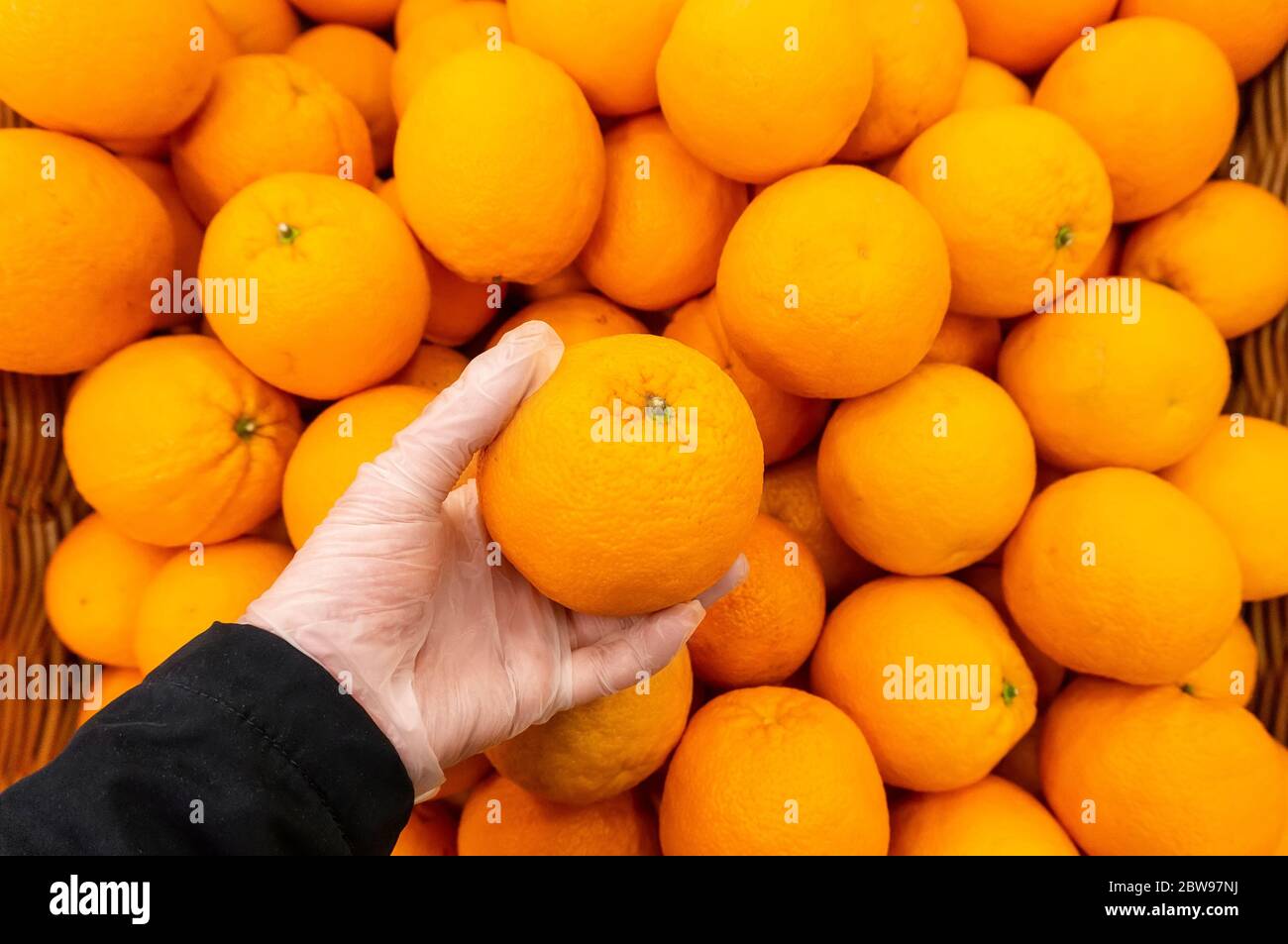Ein Kunde eines Lebensmittelladens wählt eine Orange mit einer Hand mit Handschuhen, da das Risiko einer Infektion besteht Stockfoto