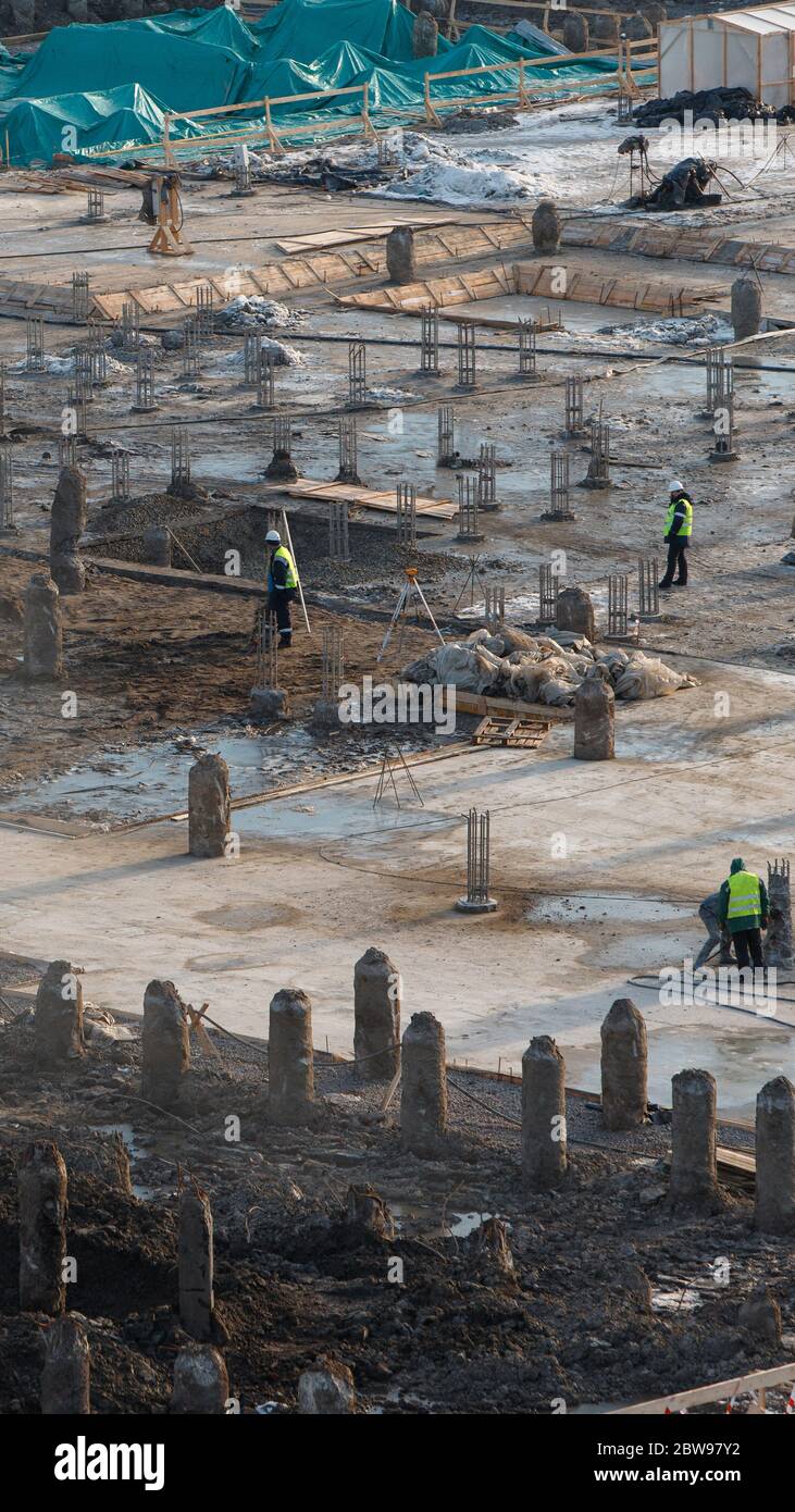 Draufsicht der Baustelle mit Stahlbetonpfählen und Arbeitern, vertikal. Arbeit an der Vorbereitung der Fundamente des Gebäudes. Stockfoto