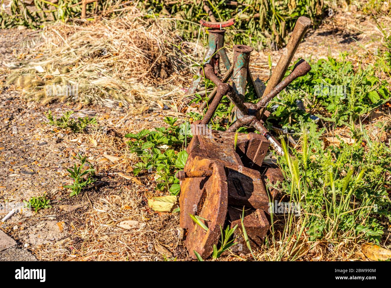 Alte, rostige Metallschrauber, Radstrebe und Achse stehen draußen im rauen Gras. Verworfene Werkstattwerkzeuge sind dem Verfall überlassen. Garage, Industrieausrüstungsabfall Stockfoto