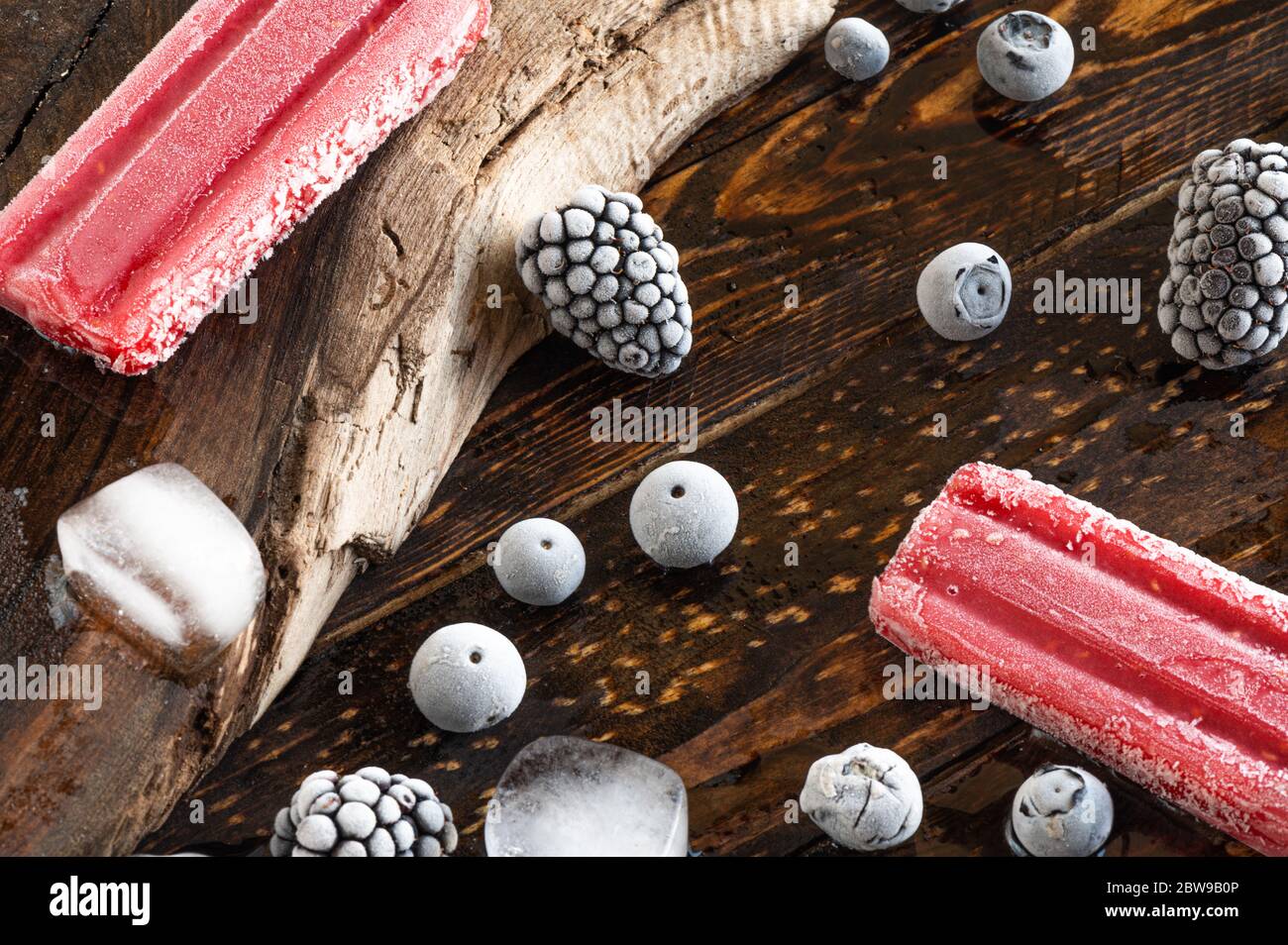Gefrorene Beeren, Eislollies und Eiswürfel über einem Holzbrett Stockfoto