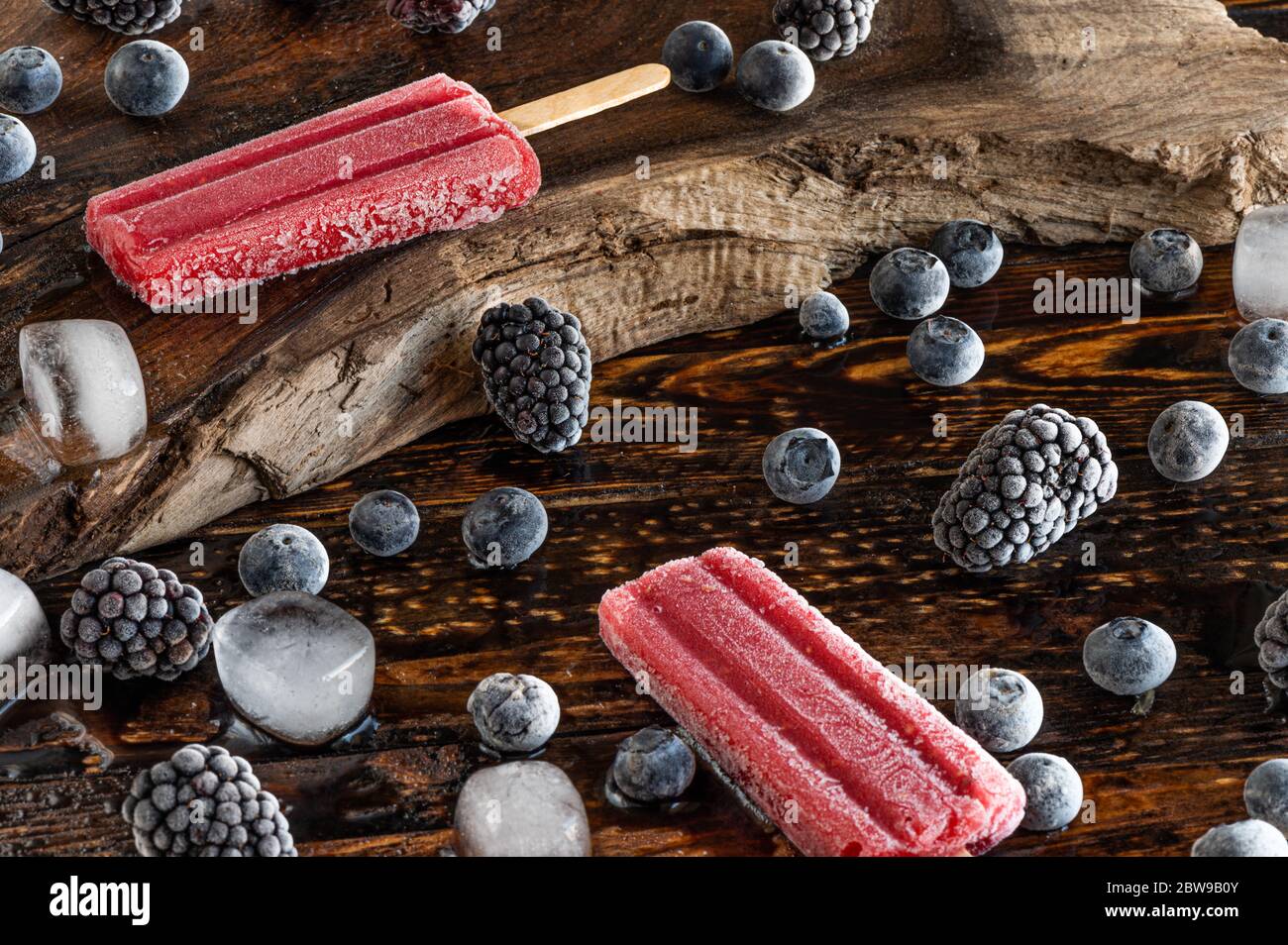 Gefrorene Beeren, Eislollies und Eiswürfel über einem Holzbrett Stockfoto