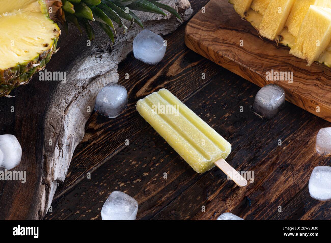 Ananas, Eislollies und Eiswürfel über einem Holzbrett Stockfoto