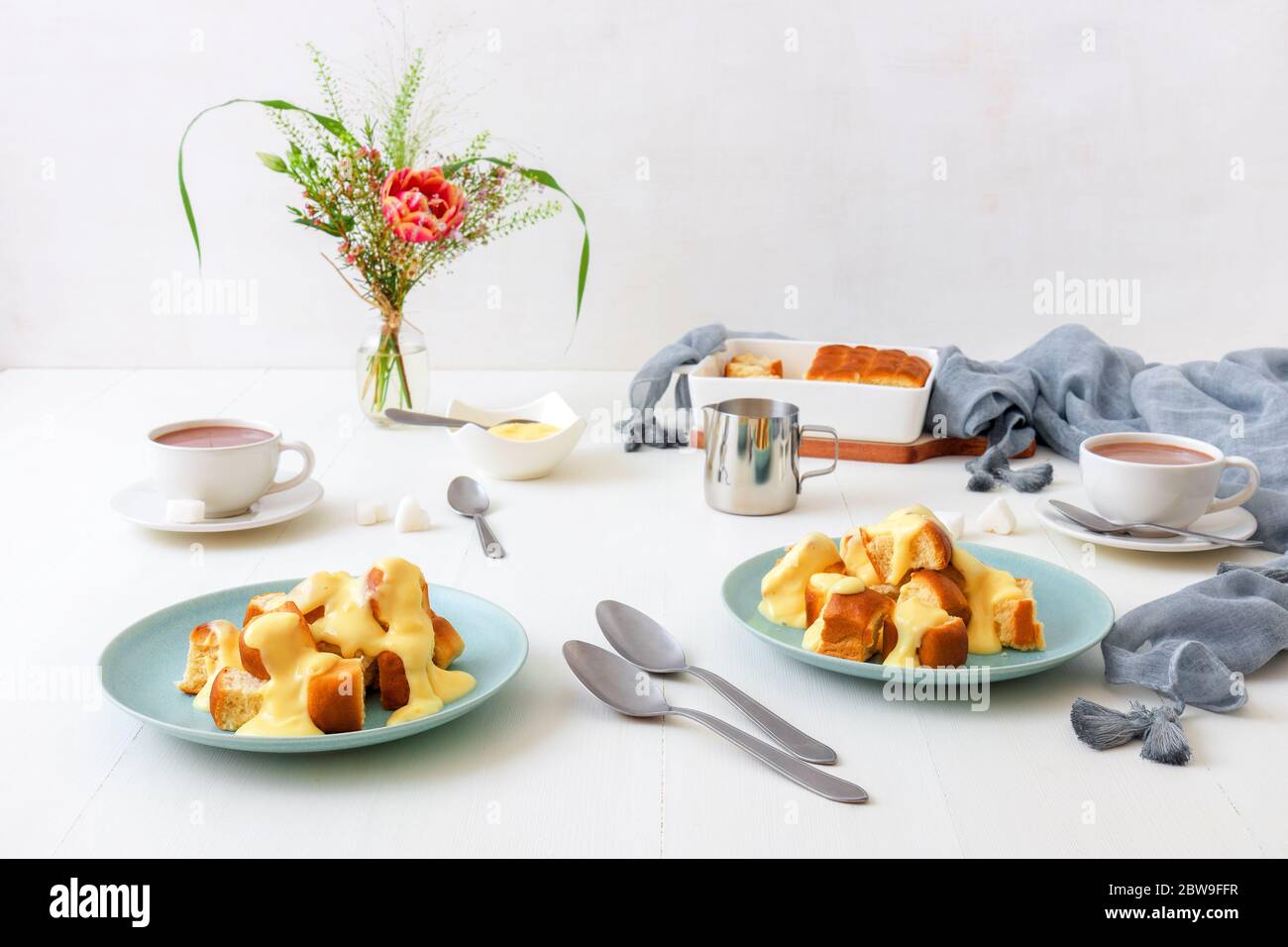 Hefepastete Brötchen mit Zabaglione oder Vanillecreme, oder Eierlikör, süßes Dessert oder Hauptgericht. Weißer Holztisch Hintergrund mit Tassen von heißem Kakao und Stockfoto