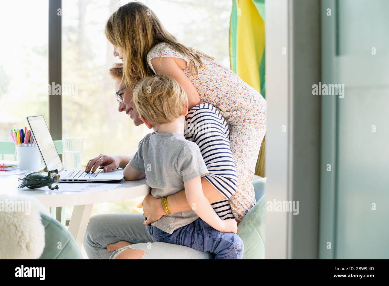 Kinder (4-5, 6-7) klettern auf ihre Mutter, während sie von zu Hause aus arbeitet Stockfoto