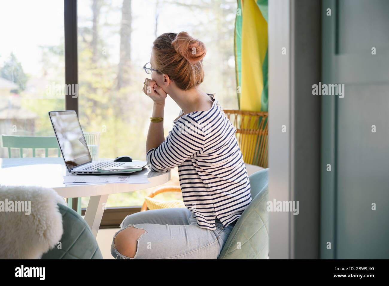 Frau, die vor dem Laptop sitzt und durch das Fenster schaut Stockfoto