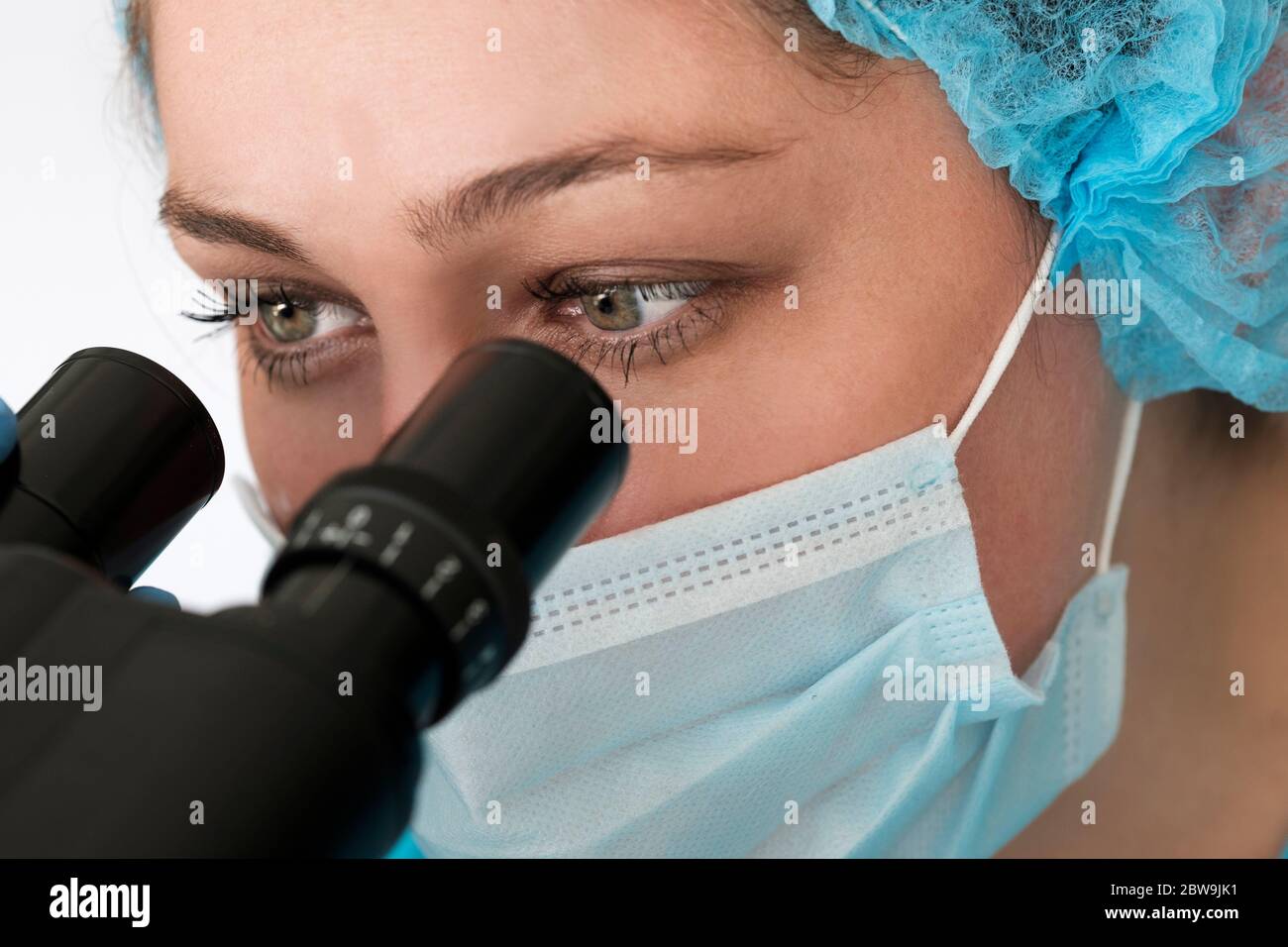 Labortechniker in Gesichtsmaske Blick durch das Mikroskop Stockfoto