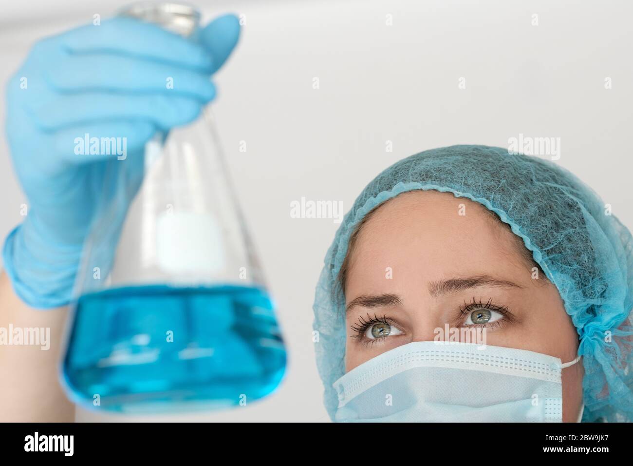 Laborant in Gesichtsmaske hält Kolben mit Flüssigkeit Stockfoto