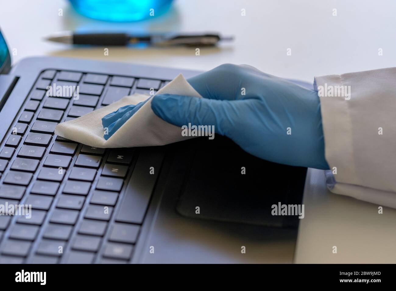 Person trägt blauen OP-Handschuh Reinigung Tastatur des Laptops Stockfoto