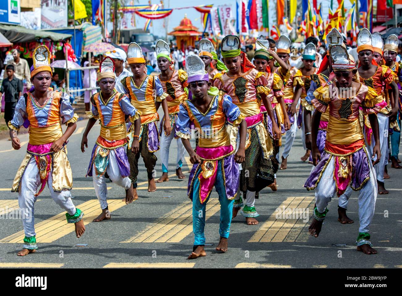 Eine Gruppe bunt gekleideter Jungen treten während der Hikkaduwa perahera in Sri Lanka entlang der Küstenstraße auf. Dies ist eine buddhistische Prozession. Stockfoto