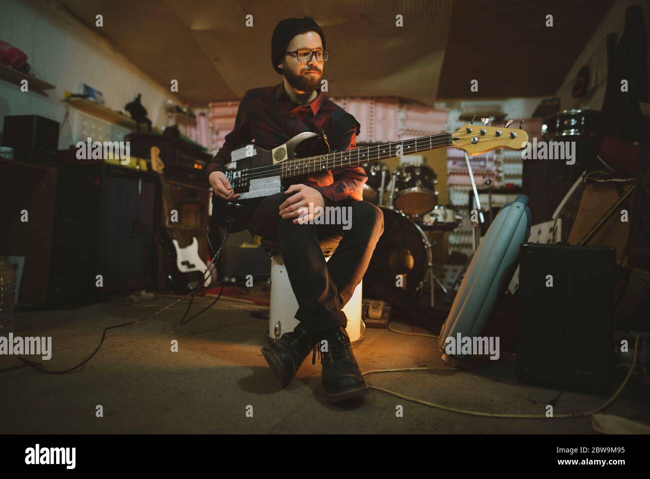 Junger Mann spielt Bass-Gitarre bei der Probe in der Garage Stockfoto