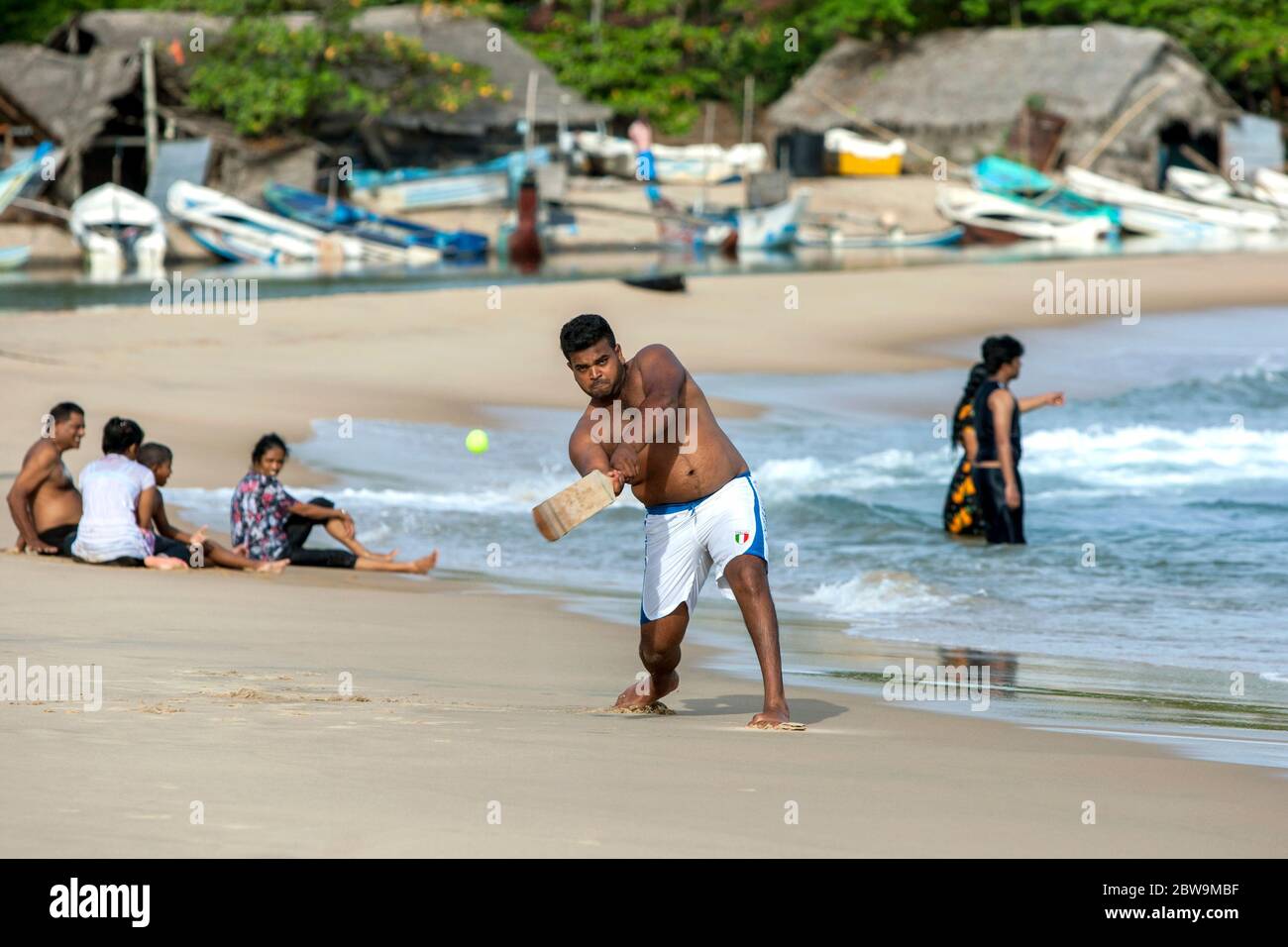 Ein Mann spielt gern einen Ball, während er Cricket am Sandstrand in Arugam Bay an der Ostküste Sri Lankas spielt. Stockfoto