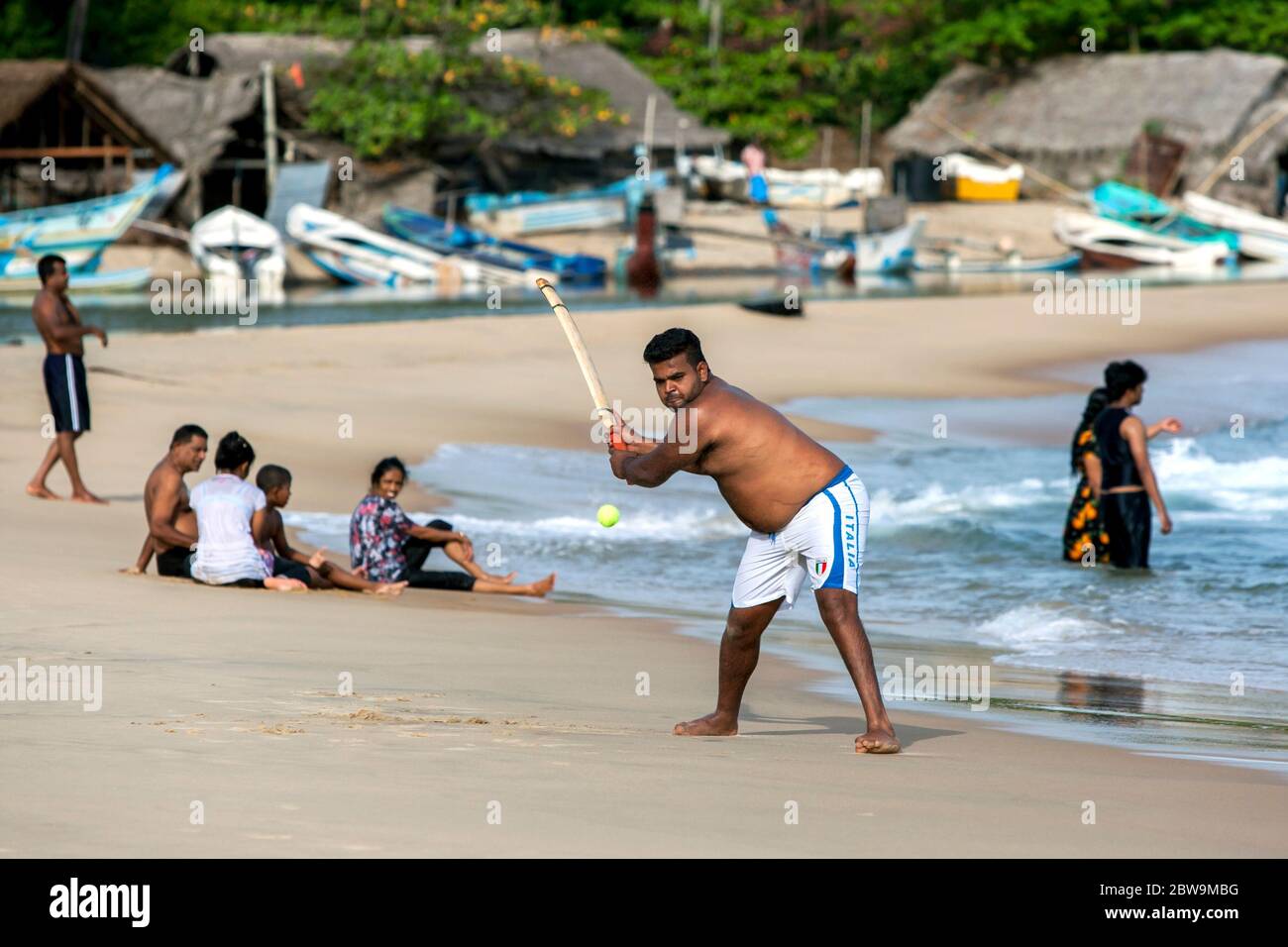 Ein Mann spielt gern einen Ball, während er Cricket am Sandstrand in Arugam Bay an der Ostküste Sri Lankas spielt. Stockfoto