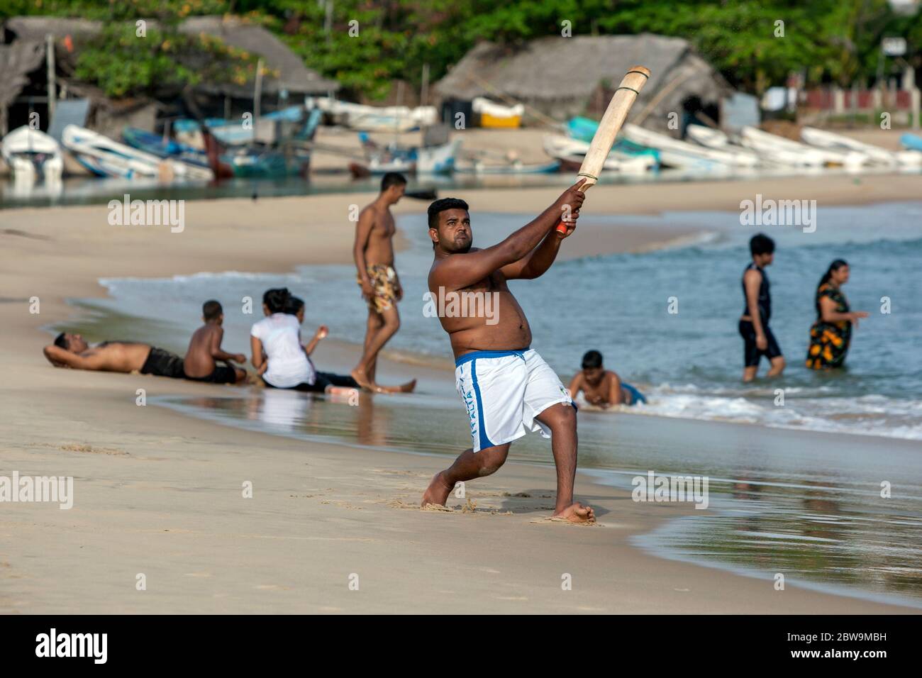 Ein Mann spielt gern einen Ball, während er Cricket am Sandstrand in Arugam Bay an der Ostküste Sri Lankas spielt. Stockfoto