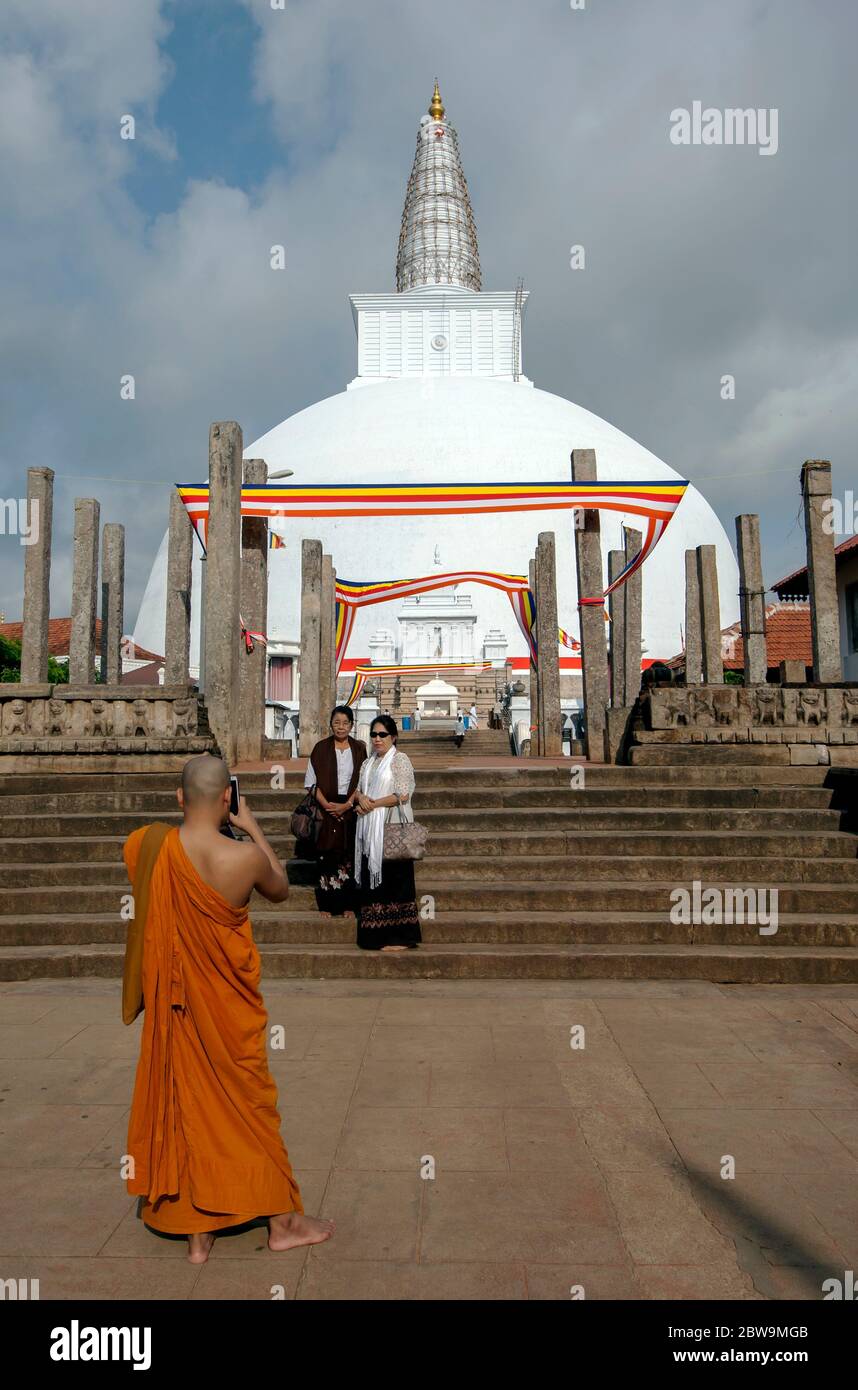 Ein buddhistischer Mönch fotografiert zwei Damen, die vor der prächtigen Ruwanwelisiya Dagoba in Anuradhapura in Zentral-Sri Lanka stehen. Stockfoto