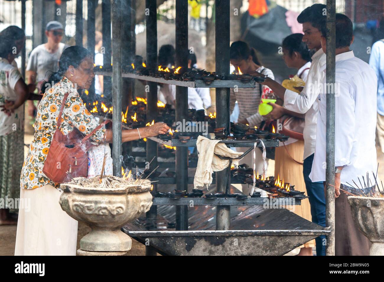 Eine Dame zündet eine Ölschale im buddhistischen Tempel des Heiligen Zahnrelikus-Komplexes in Kandy in Sri Lanka an. Stockfoto