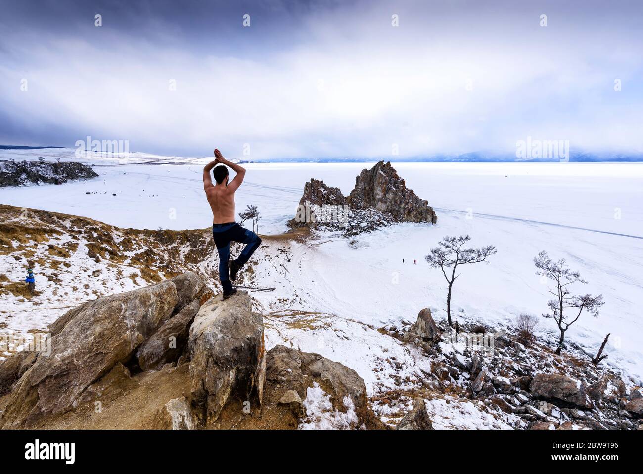 Baikalsee, Russland - 13. März 2020: Der Mensch steht am Rande eines Felsens zurück und praktiziert Yoga in der Nähe von Cape Burhan auf Shamanka Rock auf der Insel Olchon Stockfoto