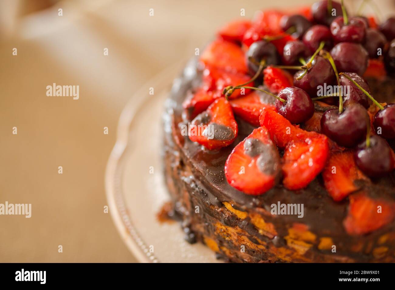 Traditionelle hausgemachte Schokoladenkuchen Süßgebäck Dessert mit brauner Glasur, Kirschen, Himbeere, Johannisbeere auf Vintage-Holz Hintergrund. Foto mit dunklen Speisen Stockfoto