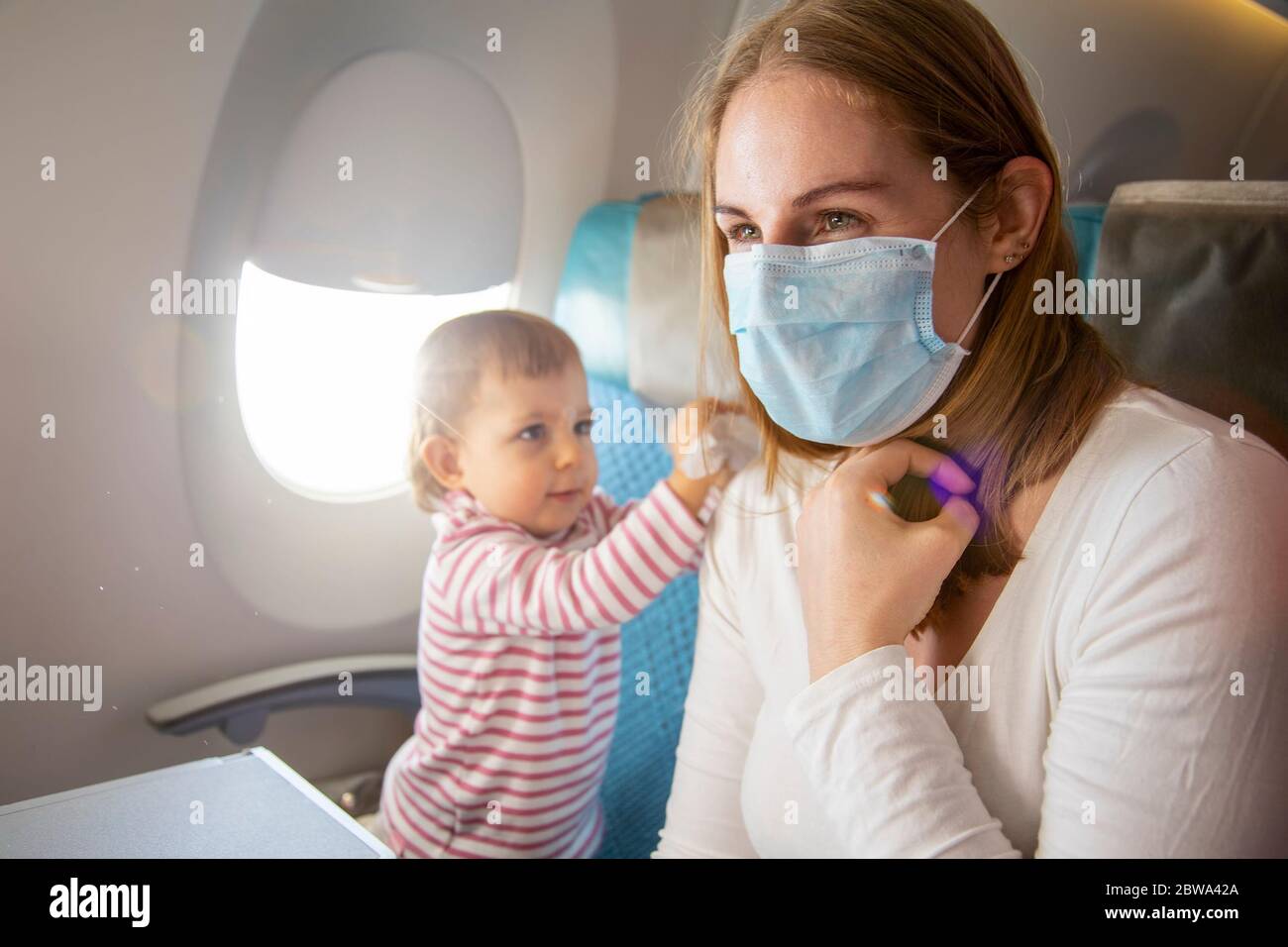 Coronavirus covid-19 asia Flight Safety Concept. Eine junge Mutter in einem Flugzeugsessel in einer medizinischen Atemmaske, sitzt ein süßes Baby neben ihr und Stockfoto
