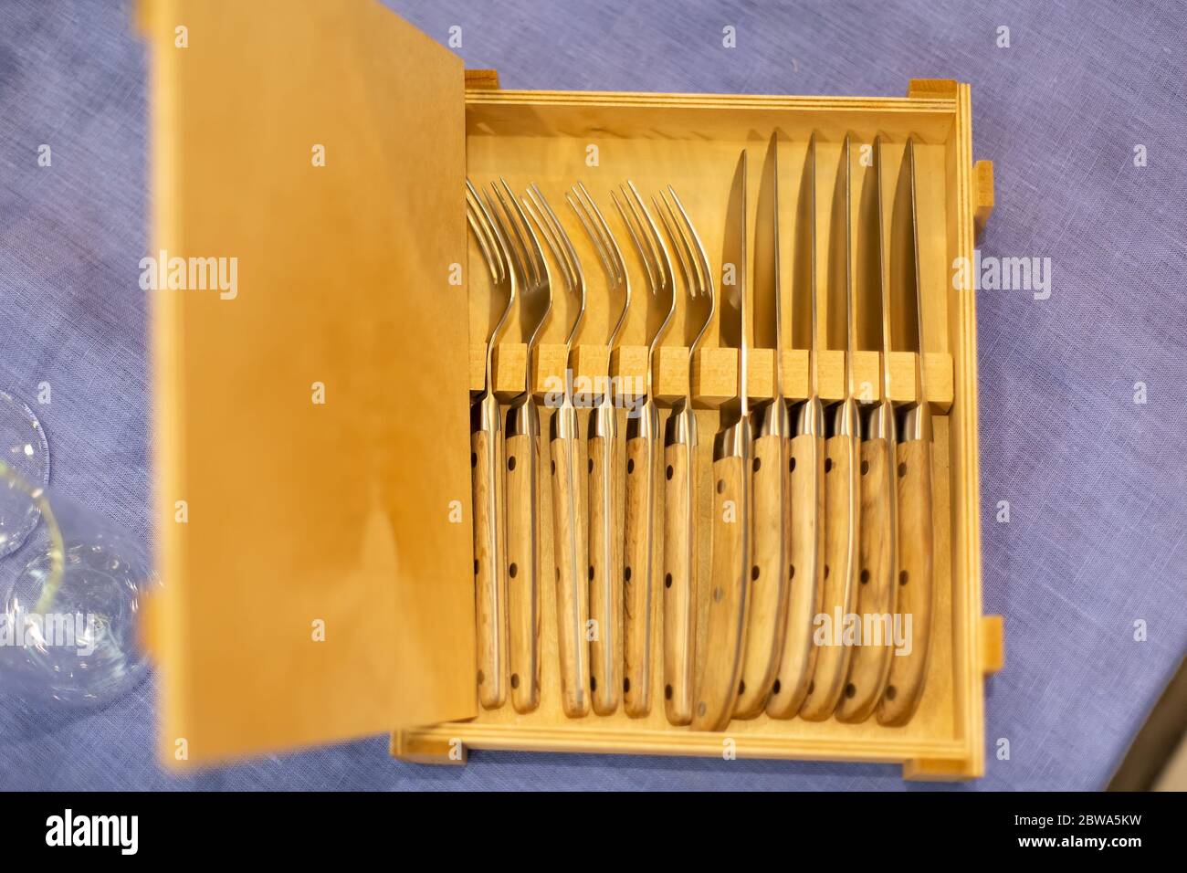Offene Holzkiste mit Besteck 6 Messer und sechs Gabeln auf einer blauen Tischdecke. Draufsicht, Nahaufnahme, weiche Fokussierung. Stockfoto