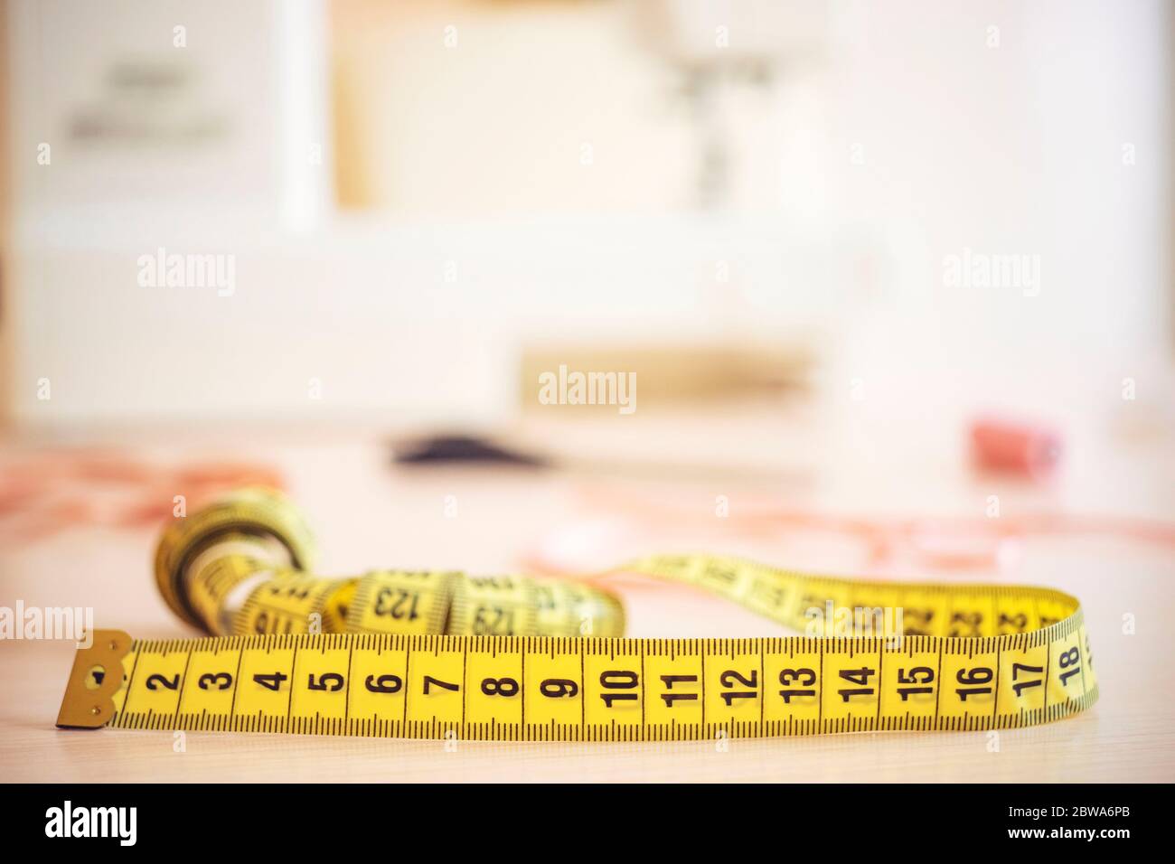 Gelbes Schneidermessgerät auf dem Desktop Näherin mit verschiedenen Accessoires auf dem Hintergrund der Nähmaschine in Unschärfe Stockfoto