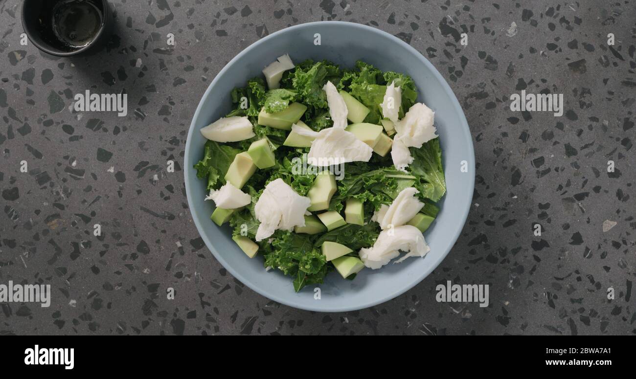 Salat von oben Mozzarella über Avocado und Grünkohl legen In blauer Keramikschale auf Betongrund Stockfoto