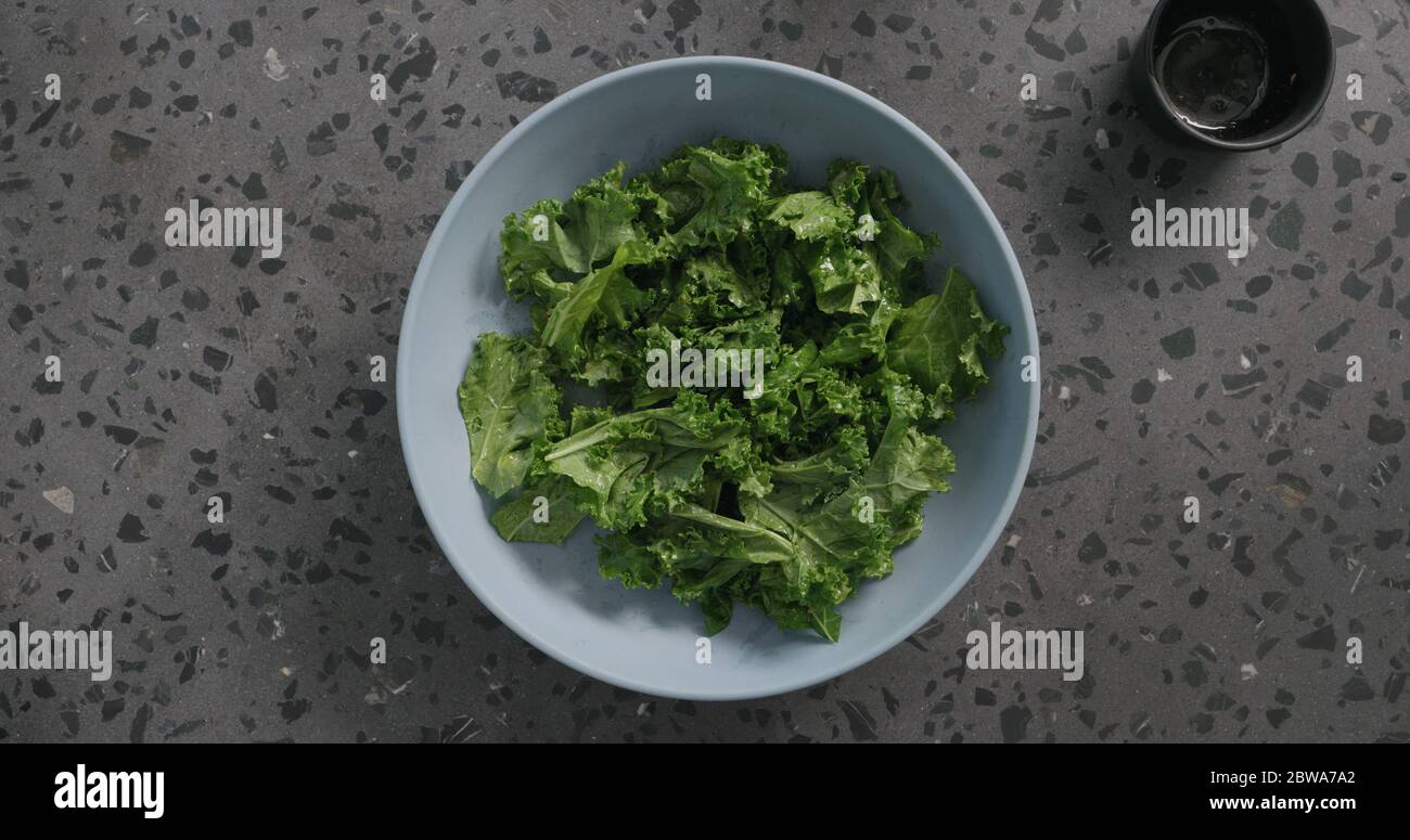 Draufsicht massierte Grünkohl-Blätter in blauer Keramikschale auf Konkreter Hintergrund Stockfoto