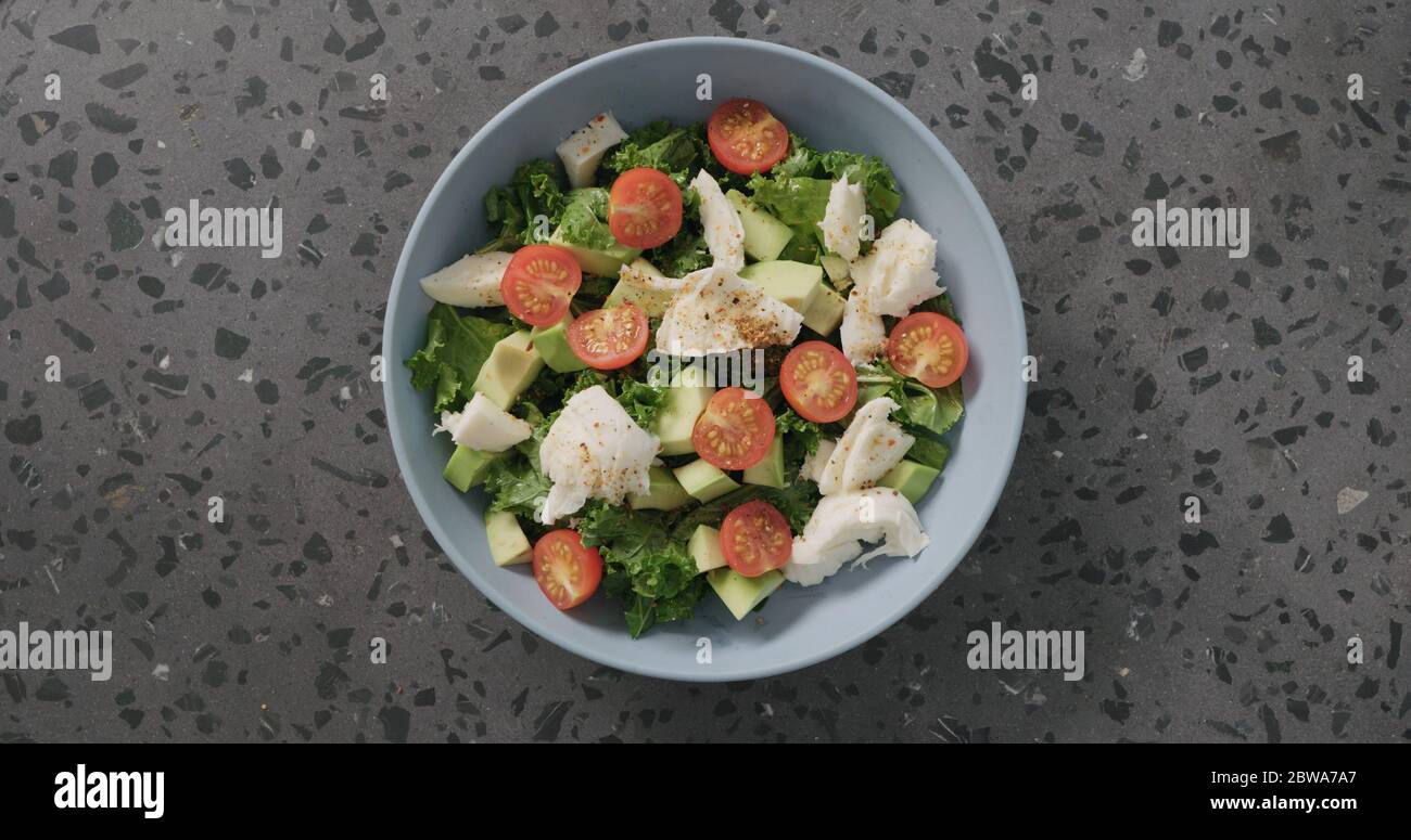 Draufsicht Salat mit Tomaten, Avocado, Mozzarella und Grünkohl in blauer Keramikschale auf Beton Hintergrund Stockfoto