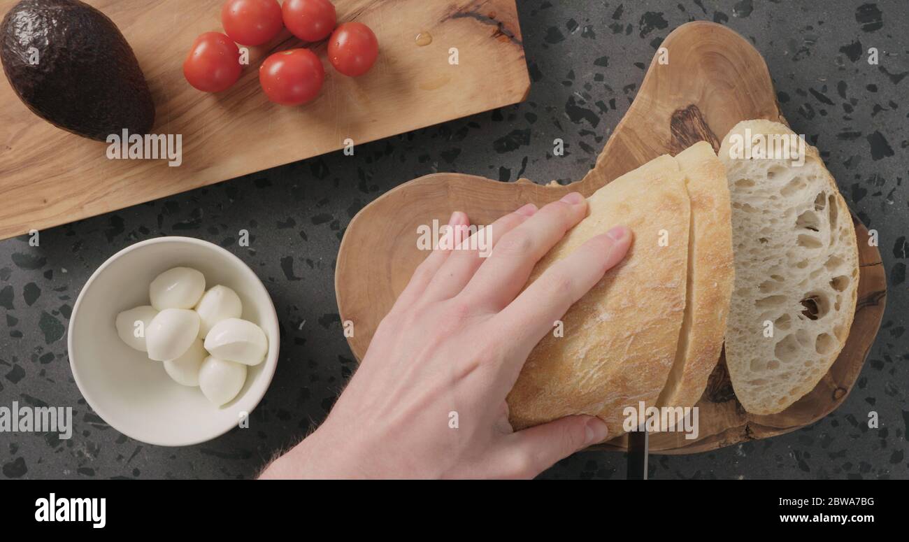 Draufsicht auf Menschenhänden, die Ciabatta-Brot auf Beton schneiden Arbeitsplatte zum Herstellen von offenen Sandwiches Stockfoto