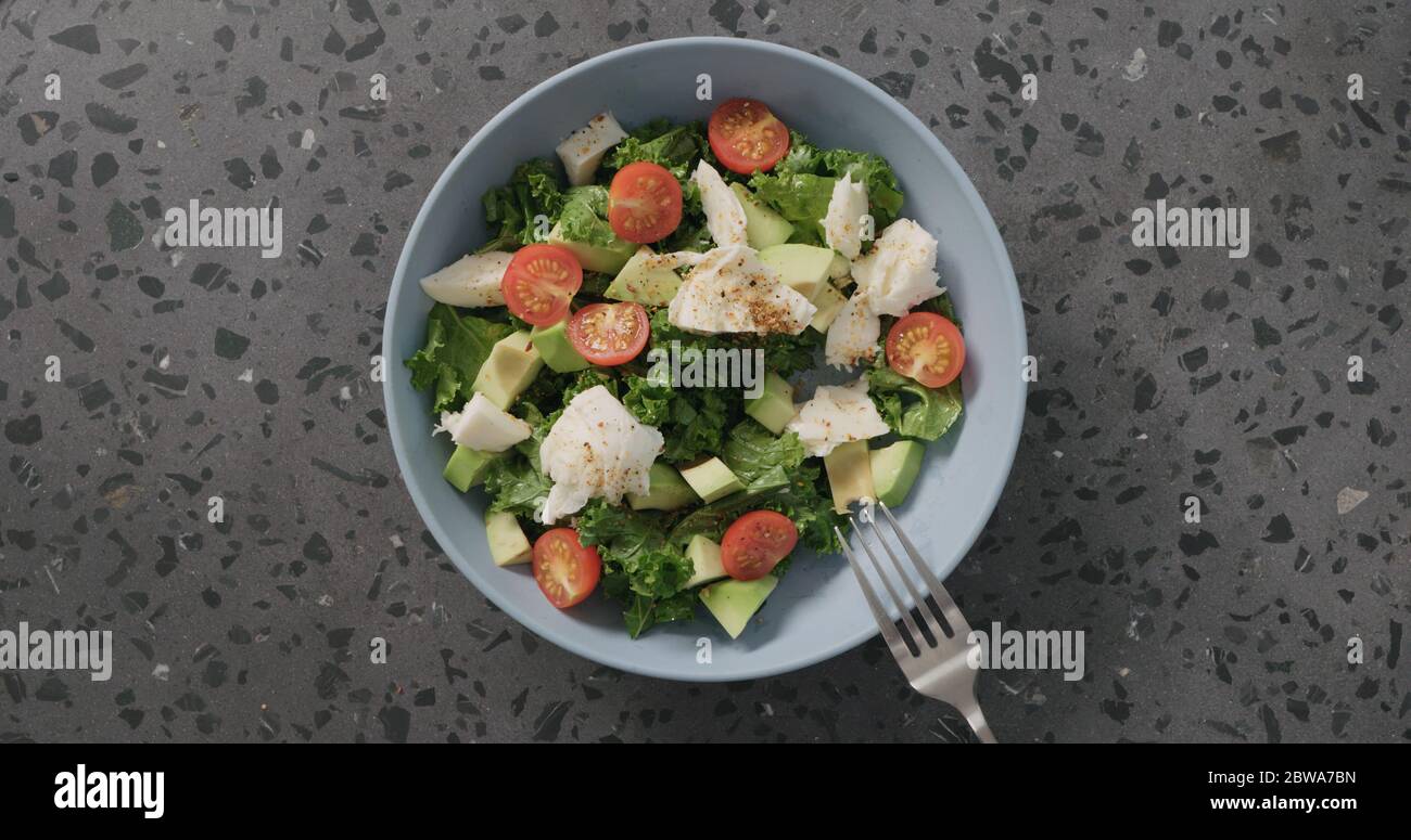 Draufsicht Salat mit Tomaten, Avocado, Mozzarella und Grünkohl in blauer Keramikschale auf Beton Hintergrund Stockfoto