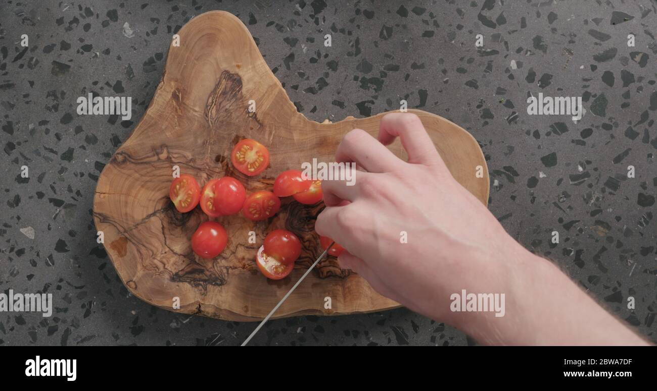Draufsicht Mann Hände schneiden Kirschtomaten auf Beton Arbeitsplatte Stockfoto