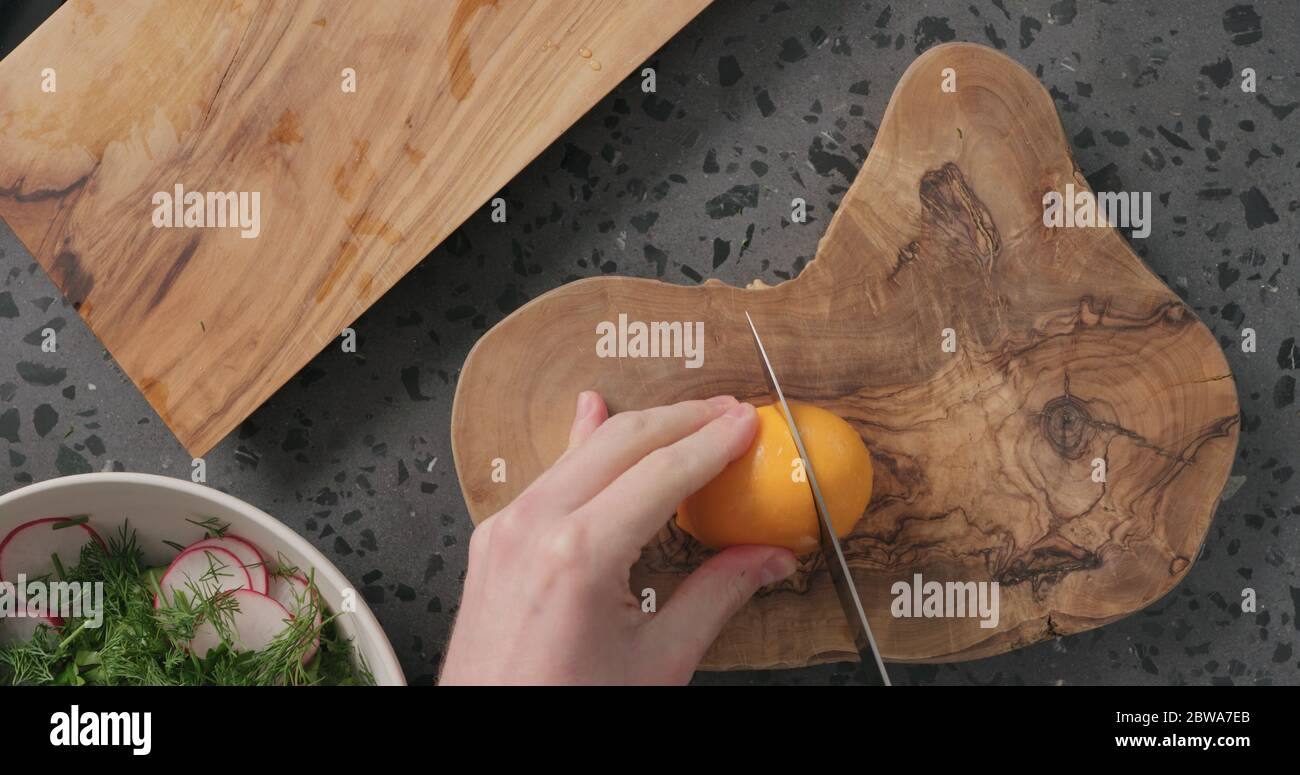 Draufsicht Mann Hände schneiden orange Zitrone auf Beton Arbeitsplatte Stockfoto