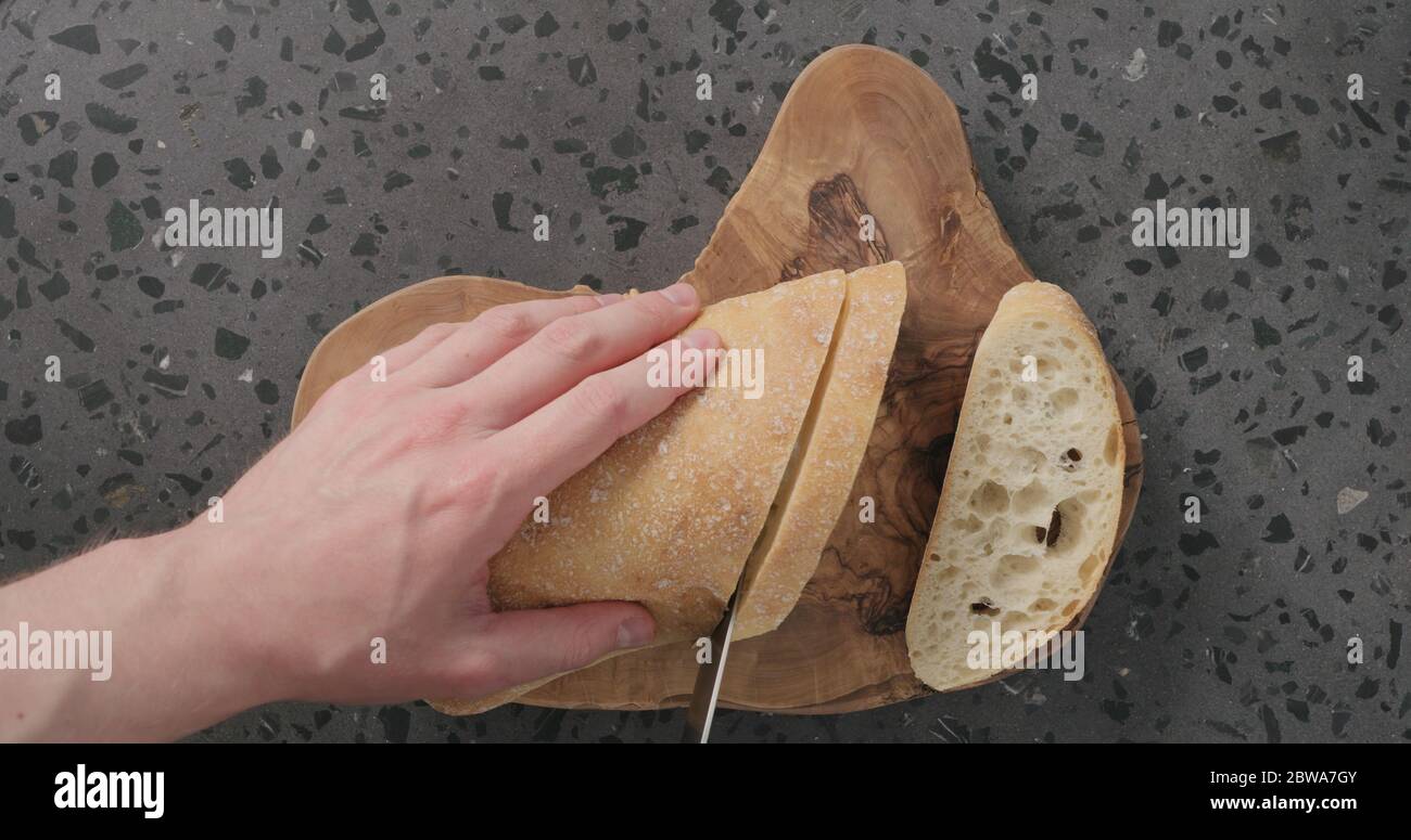Draufsicht auf Menschenhänden, die Ciabatta-Brot auf Beton schneiden Arbeitsplatte Stockfoto