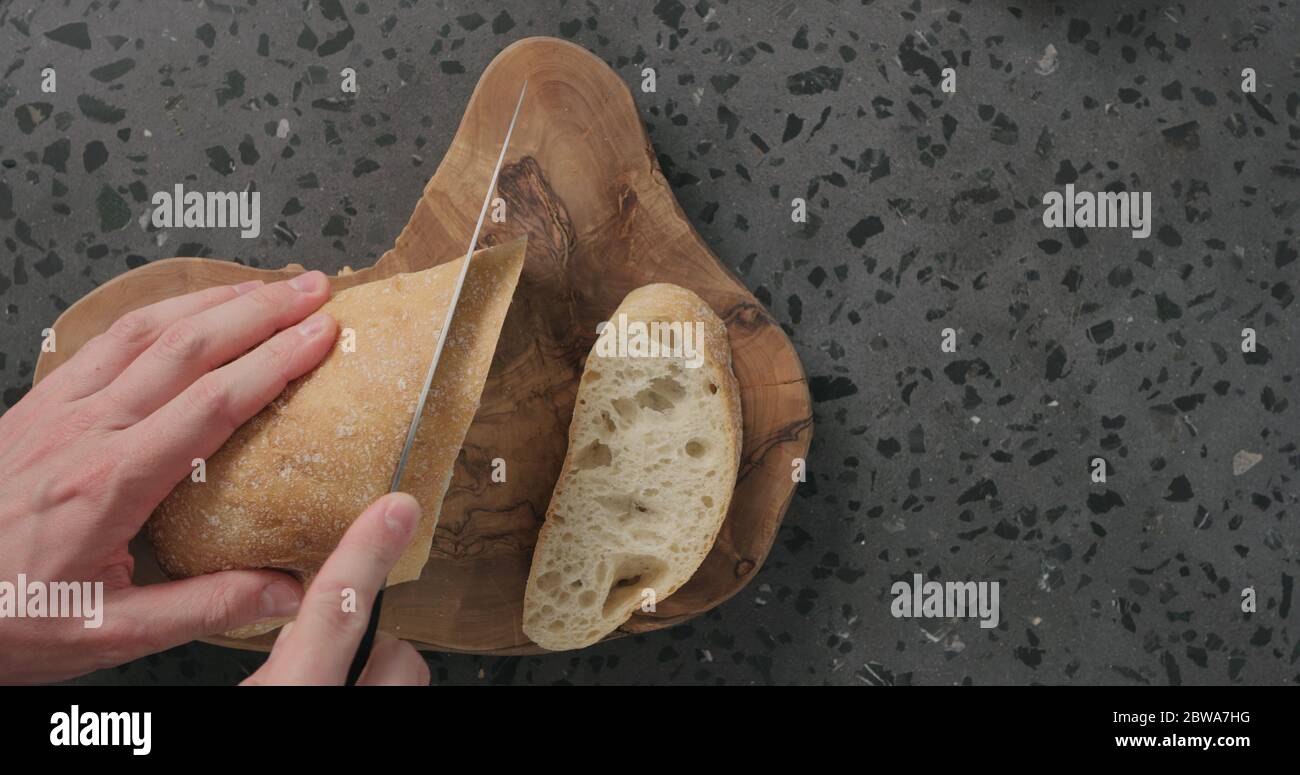 Draufsicht auf Menschenhänden, die Ciabatta-Brot auf Beton schneiden Arbeitsplatte Stockfoto