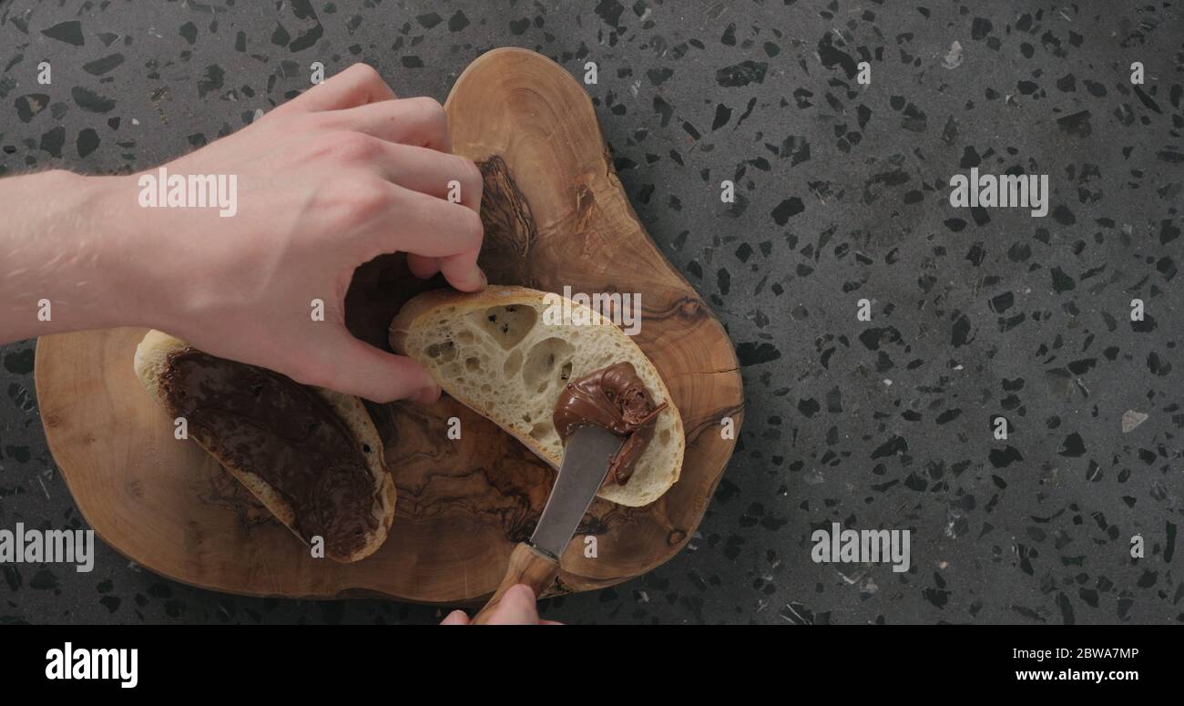 Mann verteilt Schokolade auf Ciabatta Scheibe auf Olivenbrett Draufsicht Stockfoto