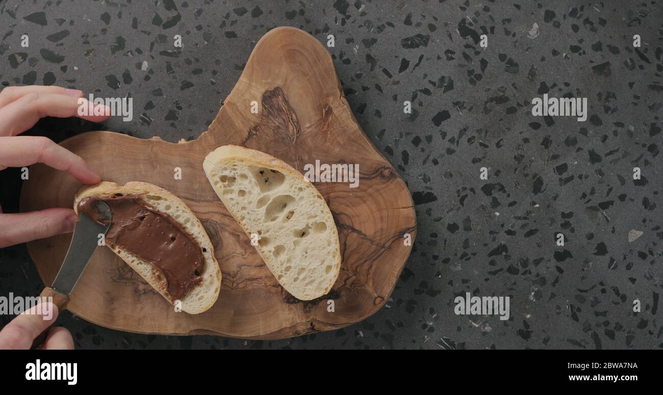 Mann verteilt Schokolade auf Ciabatta Scheibe auf Olivenbrett Draufsicht Stockfoto