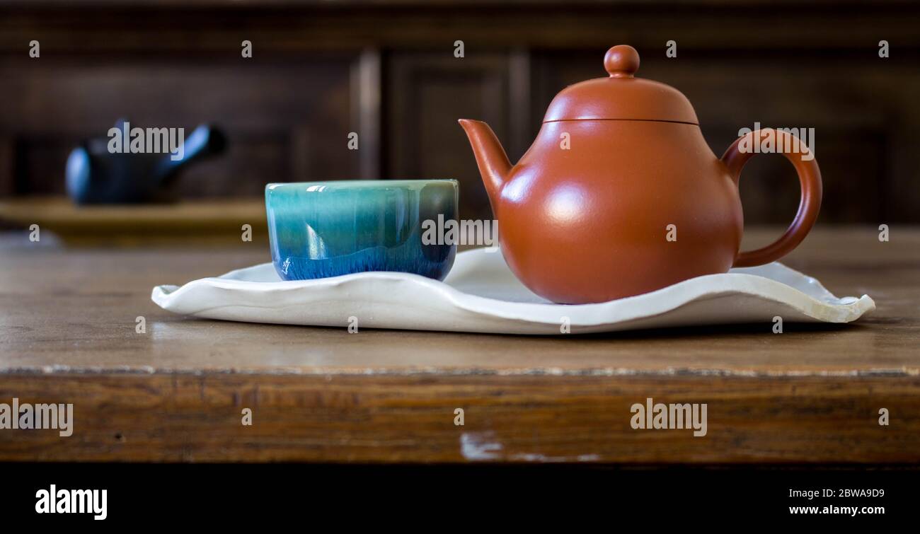 Chinesische rote Tontopf und kleine Tasse auf handgefertigten Keramik verlassen geformten Teller auf Holztisch Stockfoto