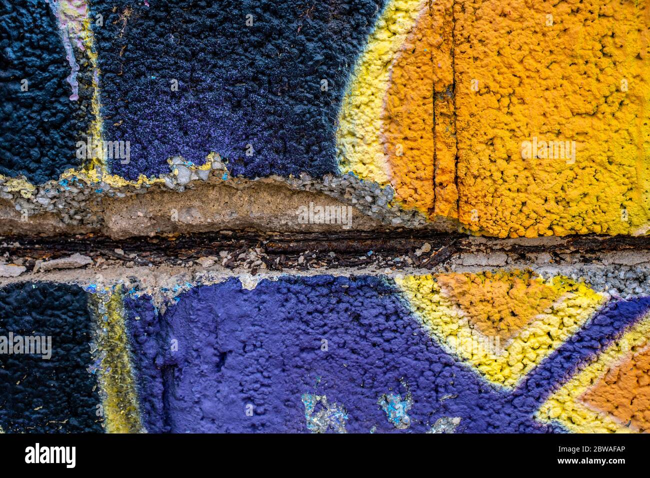 Graffiti Nahaufnahme auf gebrochenen Betonblock Wand Textur. Street Art Hintergrund. Lila, gelb, schwarz. Stockfoto