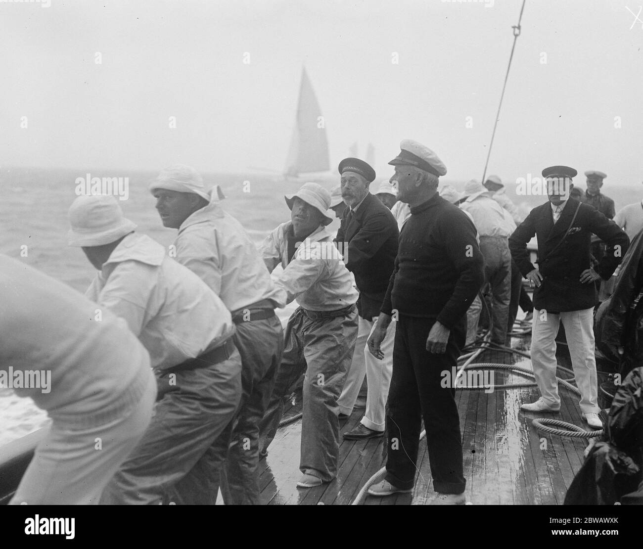 Die Kings Yacht 'Britannia in Race bei Cowes auf Isle of Wight, der Südküste von England der König unterstützt die Crew in das Großsegel zu schleppen. Rechts ist der Herzog von Connaught 2 August 1921 Stockfoto