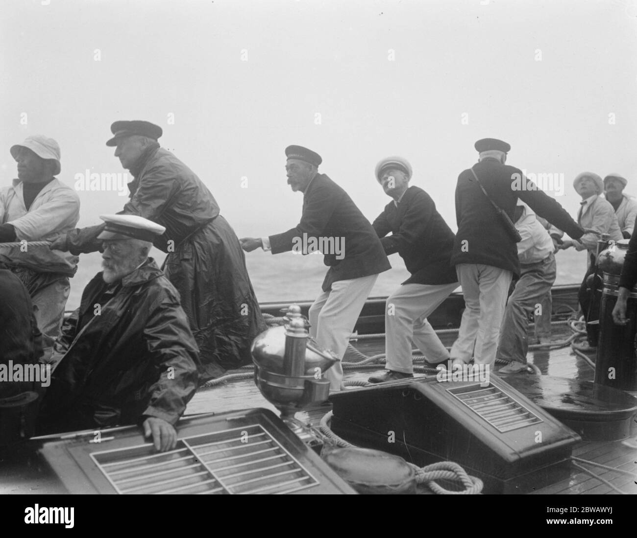 Die Kings Yacht 'Britannia in Race bei Cowes auf Isle of Wight, der Südküste von England der König und (hinter seiner Majestät) Admiral Campbell hilft der Crew, in der Main Segel zu schleppen 2 August 1921 Stockfoto