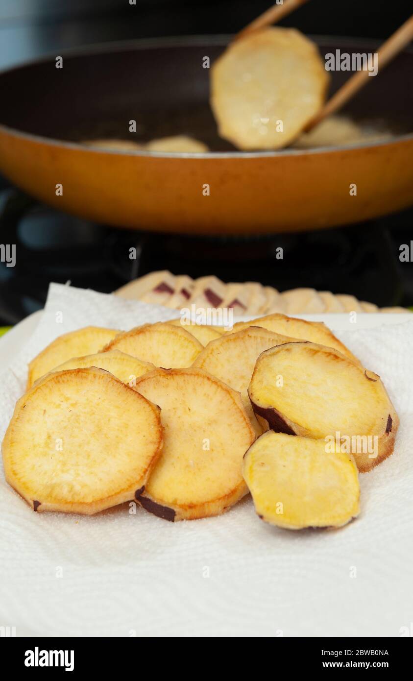 Brasilianische Küche: Hausgemachte Süßkartoffeln auf Papiertüchern. Hintergrund mit Bratpfanne und Essstäbchen. Nahaufnahme. Vertikale Aufnahme. Stockfoto