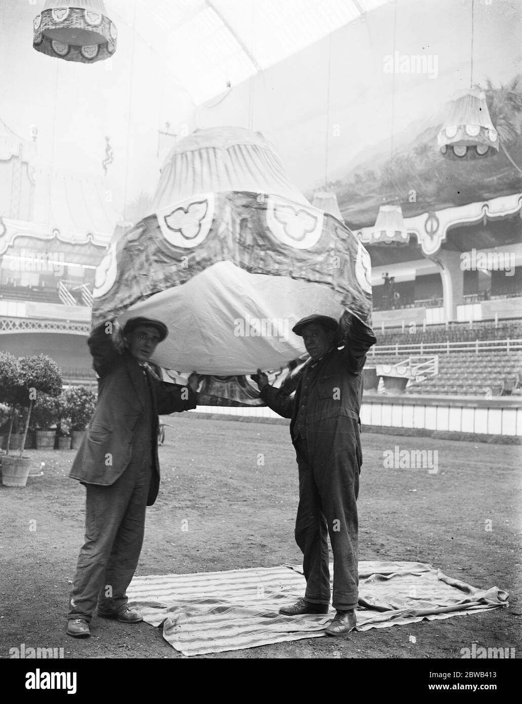 Kein Ascot Hut. Vorbereitung auf die Internationale Pferdeschau in Olympia zwei Arbeiter, die sich mit den Dekorationen beschäftigen, werden hier gesehen, wie sie einen der riesigen Lampenschirme am 20. Juni 1923 über ihren Köpfen halten Stockfoto