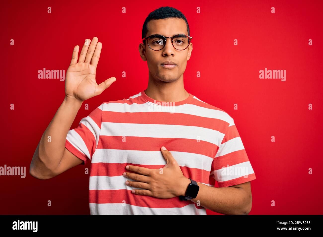 Junge gut aussehende afroamerikanischen Mann in lässig gestreiften T-Shirt und Brille mit der Hand auf der Brust und offene Handfläche, so dass ein Loyalitätsversprechen Hafer Stockfoto