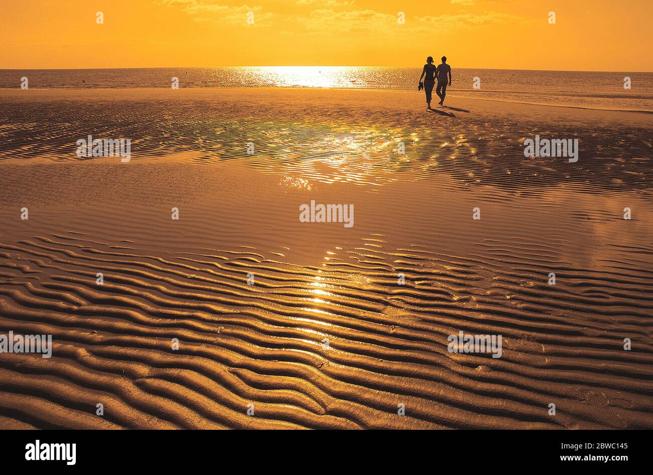 Paar wandert bei Ebbe am Strand, Sonnenuntergang, MR: JA Stockfoto